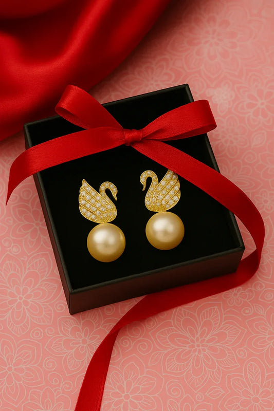 Gold earrings with pearl centers in a black box tied with a red ribbon on a pink floral background