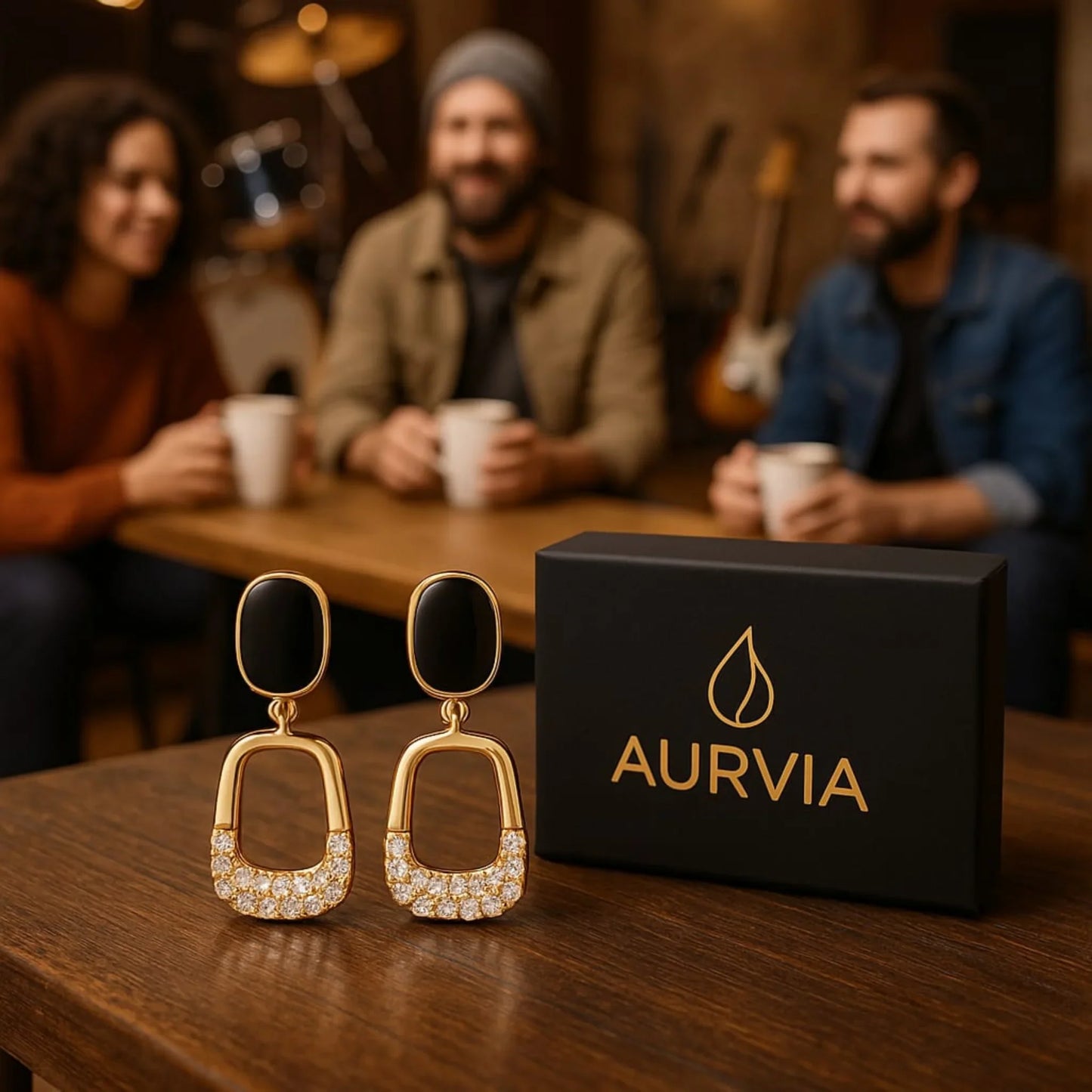 Gold earrings with black stones on a table in front of a box labeled 'Aurvia' with people sitting at a table in the background.