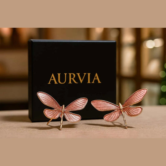 Rose gold butterfly earrings in front of an Aurvia box on a beige surface.