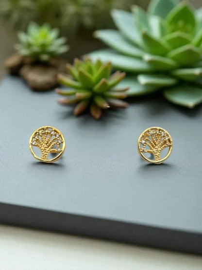 Gold tree-shaped earrings on a dark surface with succulents in the background